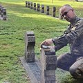 Soldat kniet und reinigt ein Grabkreuz aus Stein.