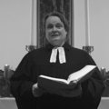 Eine Frau im Talar steht mit einem Buch vor einem Altar.